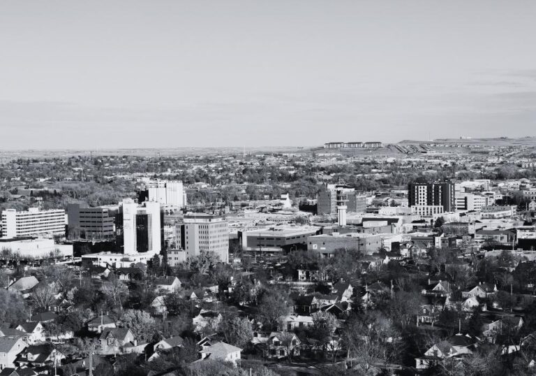 Black-and-white aerial view of downtown Rapid City, South Dakota, showing commercial buildings, neighborhoods, and the surrounding landscape.