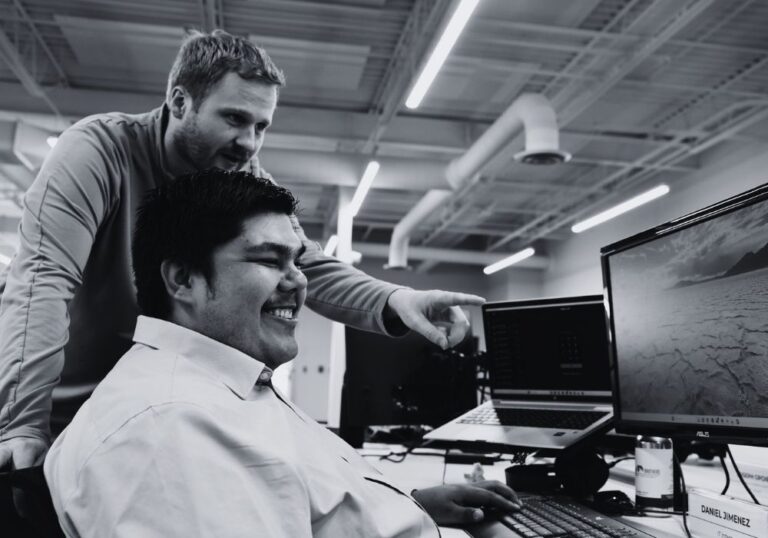 Two IT team members collaborating at a computer workstation in an office.