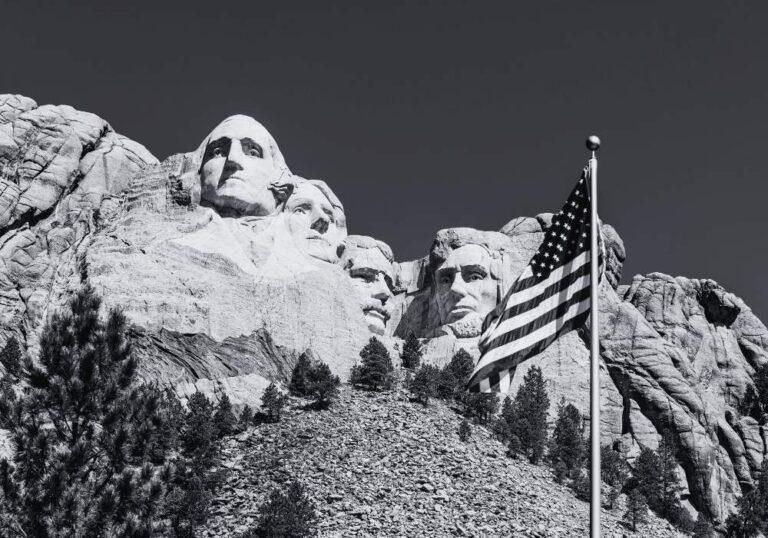 Black-and-white view of Mount Rushmore National Memorial in South Dakota with an American flag in the foreground.
